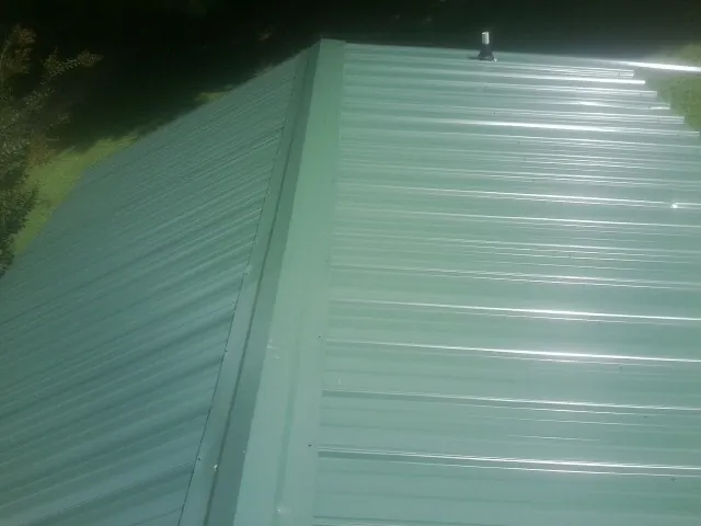 New green metal panels meeting at the ridge of a roof — Flat Roof Repair work by our crew in Cicero