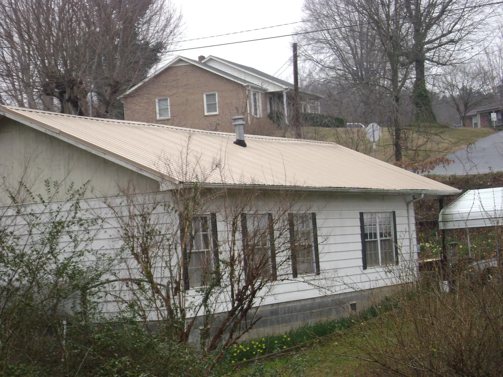 Tan metal roof on a white sided house set into a hillside — Commercial Roofing by Roofing Brothers in Cicero